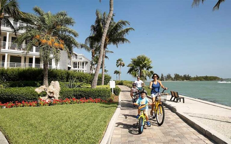 family on bikes riding along coastal wall path beside condo buildings at south seas island resort captiva sanibel fort myers