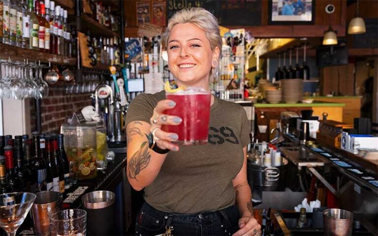 female bartender smiling handing out cocktail in bar area at the standard restaurant fort myers