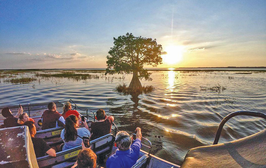 group on airboat tour with sunset over lake and cypress tree boggy creek adventures