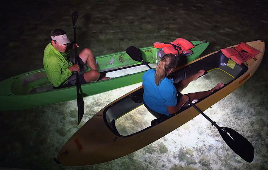 man and woman in kayaks with clear bottoms and lights showing underwater night kayaks key west