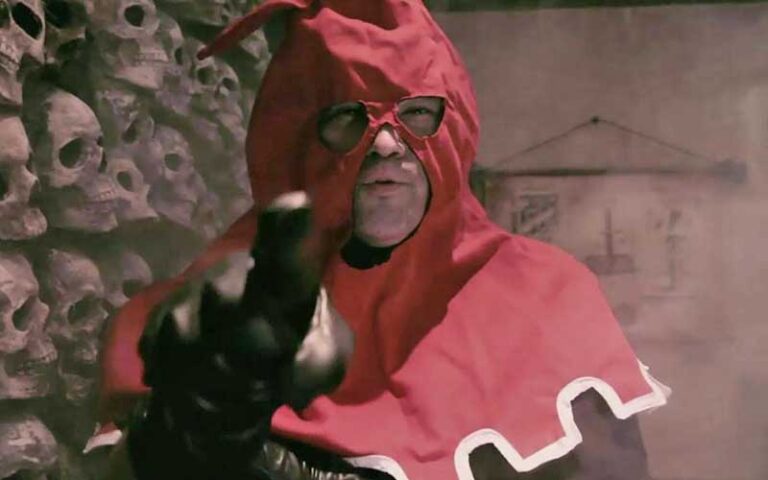 man in red executioner hood holding axe with wall of skulls at medieval torture museum st augustine