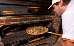 man sliding pizza into brick oven at carmelos pizzeria st augustine