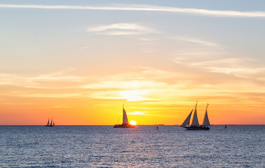 orange and yellow sunset over water with catamarans and sailboats mallory square key west