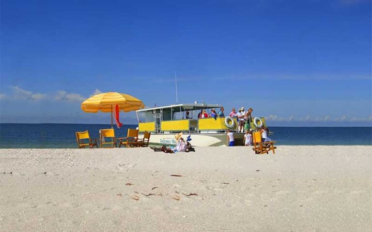 pontoon boat moored off beach with chairs and umbrellas at adventures in paradise fort myers