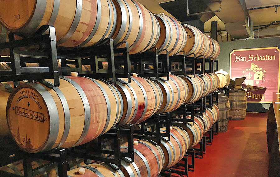 rows of oak barrels in warehouse with sign san sebastian winery st augustine