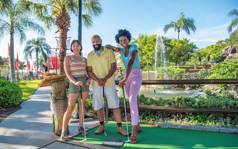 three golfers smiling with pirate ship behind at smugglers cove adventure golf fort myers beach