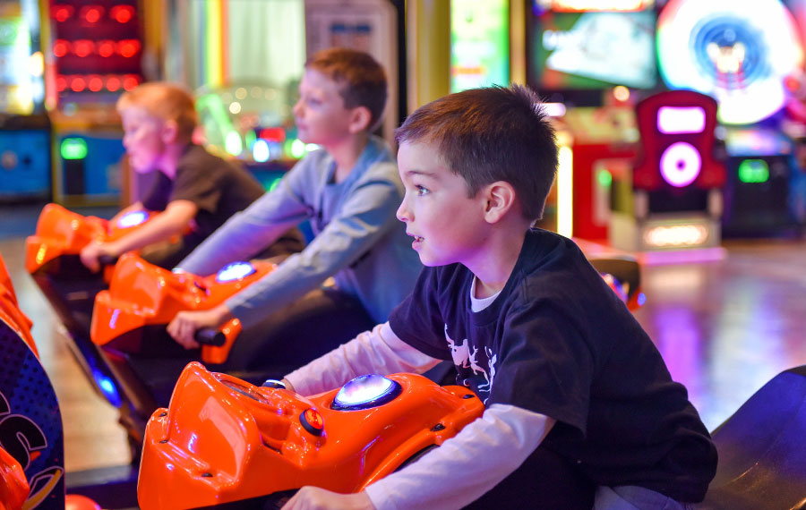 three young boys competing on a motorcycle racing arcade game