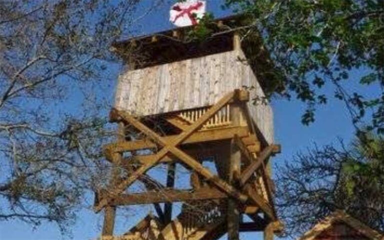 wooden lookout tower with spanish flag above trees at colonial quarter st augustine