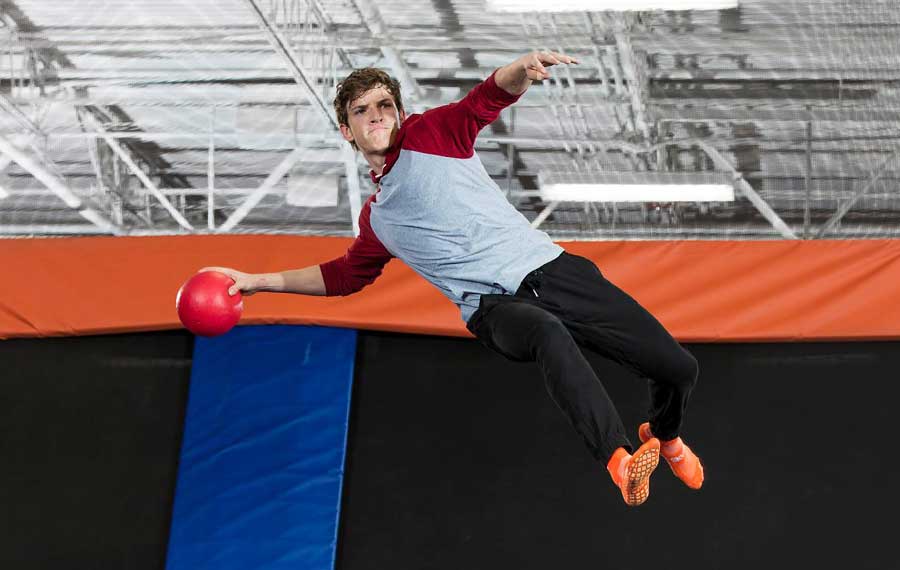 boy with dodgeball in hand and orange socks bouncing above trampoline to throw sky zone fort myers