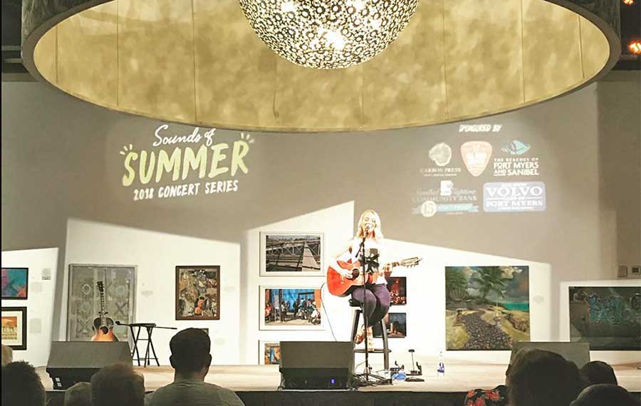 guitarist on stage with art on walls light globe and audience sidney and berne davis art center fort myers