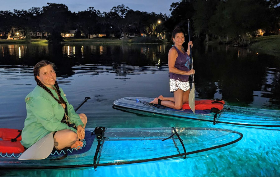 ladies on clear paddleboards with blue glow lights on lake at night at epic paddle adventures orlando