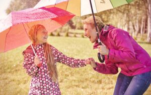 mother and daughter with umbrellas laughing in rain