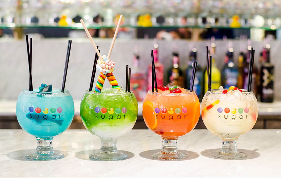 row of colorful drinks with candy garnish on marble countertop at sugar factory icon park orlando