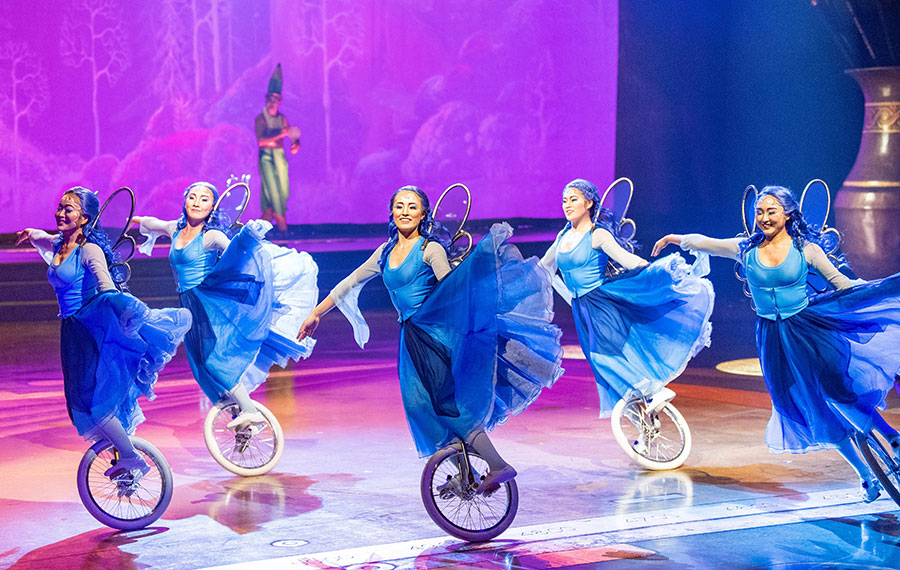 troupe of acrobats in blue dresses on unicycles dancing on stage at drawn to life disney springs
