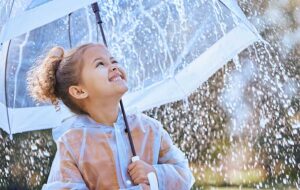 young girl squinting up at umbrella in the rain