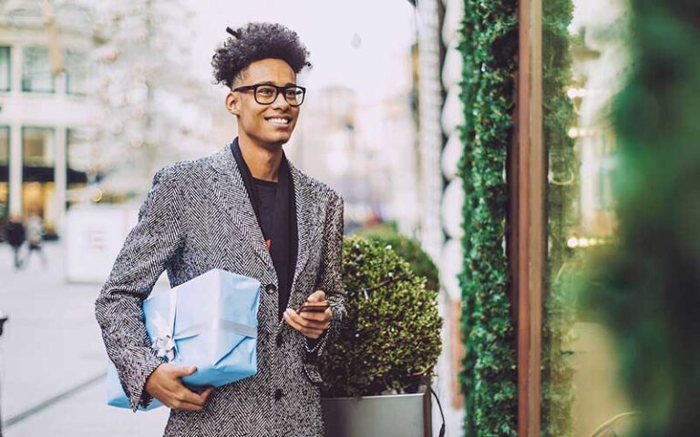 young man dressed in fashionable coat with gift under arm at edison mall fort myers