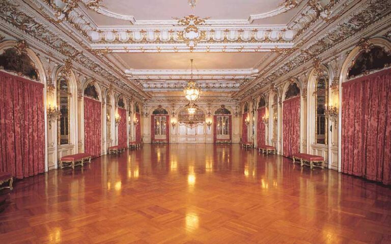 beautiful grand ballroom with wood floors and red curtains at henry morrison flagler museum palm beach