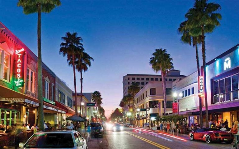 busy palm lined street with crowds and neon signs at night at clematis street west palm beach