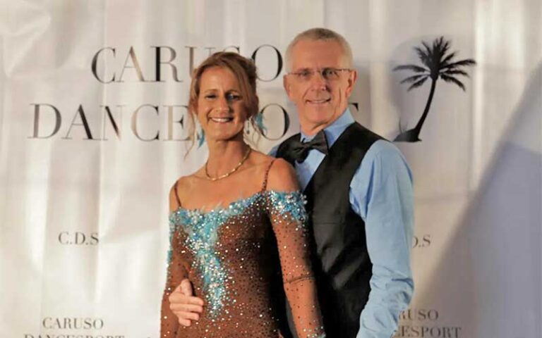 couple dressed for ballroom competition with studio logo backdrop at caruso dancesport west palm beach