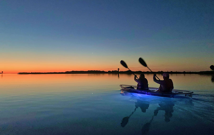 couple in illuminated kayak paddling toward setting sun over dark water at get up and go kayak shell key reserve tampa