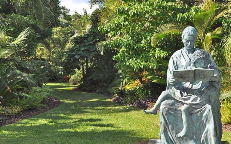 garden path through trees with statue of woman reading book to child on her lap at mounts botanical garden west palm beach