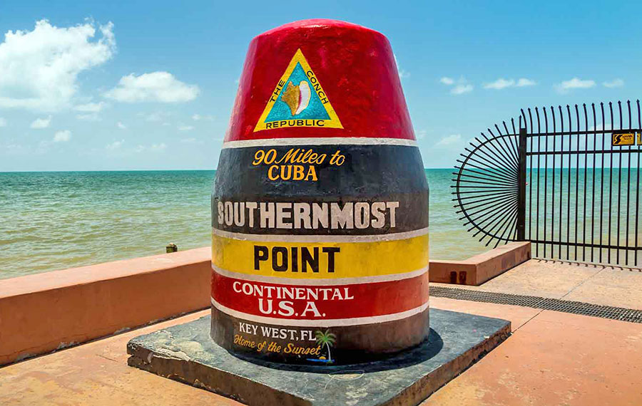 iconic southernmost point marker with cloudy sky green water key west