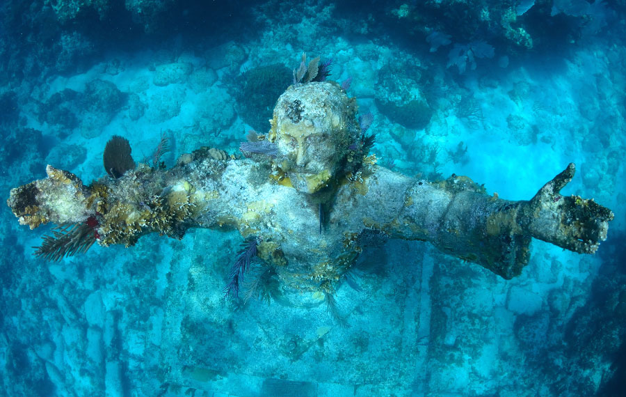 underwater statue viewed from above of saintly figure with arms extended and face lifted with coral growth christ of the deep key largo