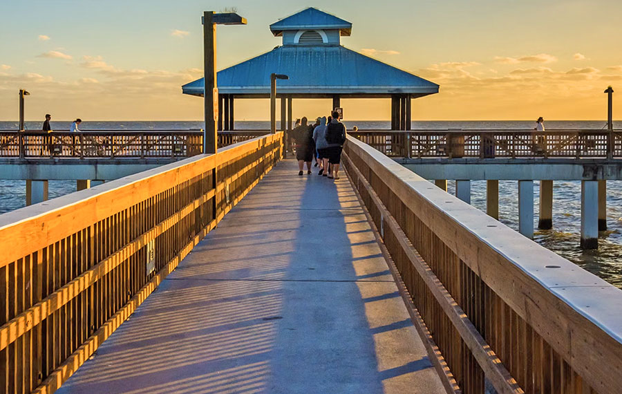 beachgoers walking along fishing pier at fort myers with sunset glow from right side