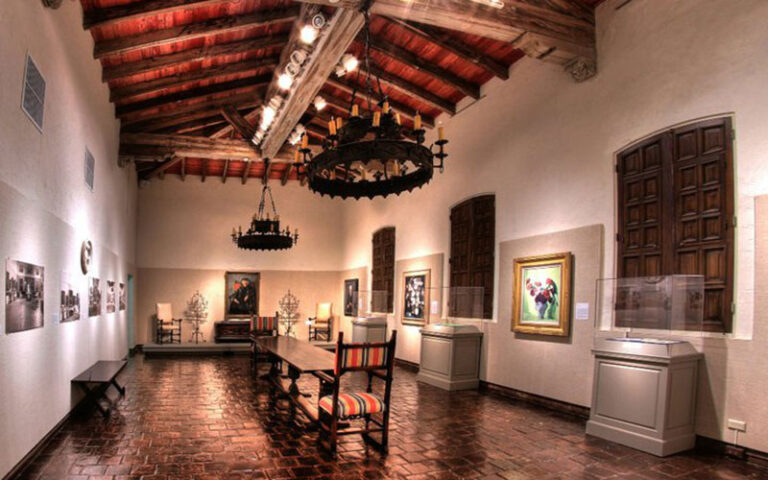 interior of spanish colonial room with open timber ceiling and art exhibits at society of the four arts palm beach