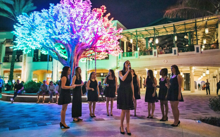 ladies group singing in courtyard with multi colored lighted tree at night at the square west palm beach