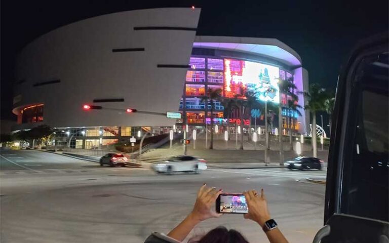 nighttime view of kaseya center with tourist holding up cameraphone at open miami bus tours