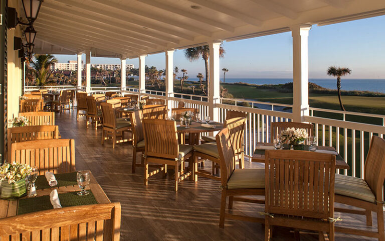 patio seating on clubhouse veranda overlooking golfing green and shoreline at palm beach par 3 golf course