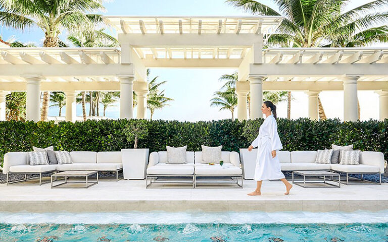 robed woman walking along poolside with seating at the spa at the breakers palm beach