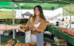 woman buying vegetables under green awning at west palm beach greenmarket