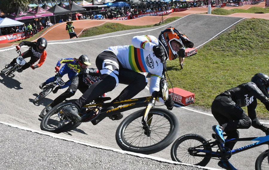 bmx bike racers rounding half pipe curve on track with event tents in background at okeeheelee park west palm beach