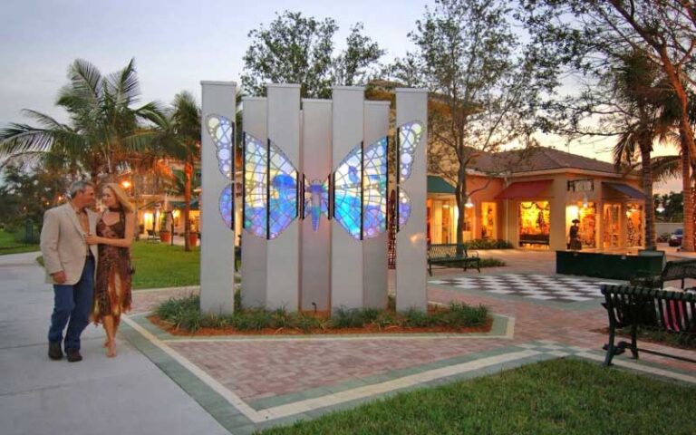 butterfly sculpture in grassy area at twilight with shops and couple at pga commons art dining district palm beach gardens