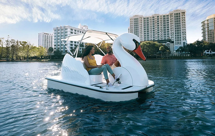 couple pedaling swan boat on lake with buildings and clear sunny sky lake eola orlando