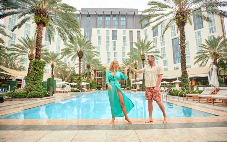 couple standing along edge of pool in courtyard hotel area with palms at hilton west palm beach