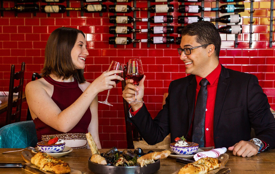 couple toasting red wine seated at restaurant table with food entrees at mias italian kitchen orlando