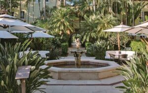 exterior of hotel shrouded in trees with courtyard fountain at the brazilian court hotel palm beach