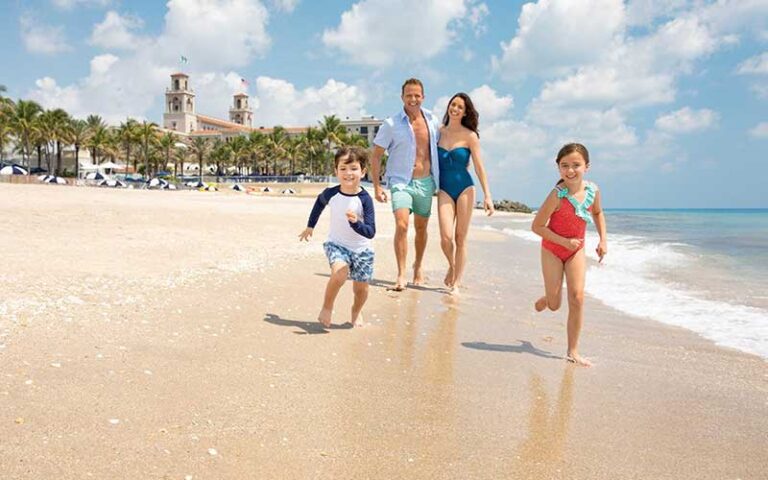 family of four running along beach with hotel in background at the breakers palm beach
