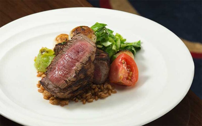 filet mignon with pine nuts and roasted onion and tomato on white plate at flagler steakhouse palm beach