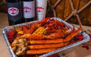 foil tray full of crab legs and seasoned items with wine bottles at mr mrs crab juicy seafood bar orlando kirkman