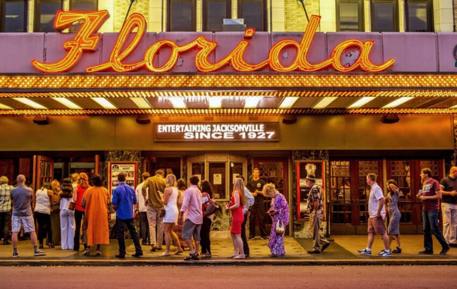 line of people under marquee sign at night with neon word florida at florida theatre jacksonville