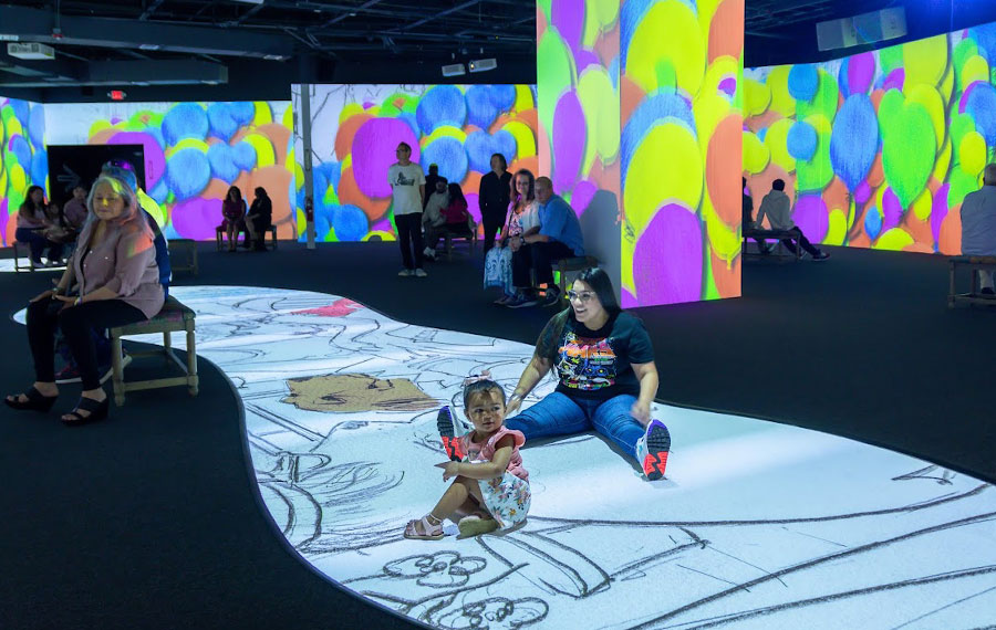 mom and toddler sitting on projection floor with video playing on walls at lonely dog immersive orlando