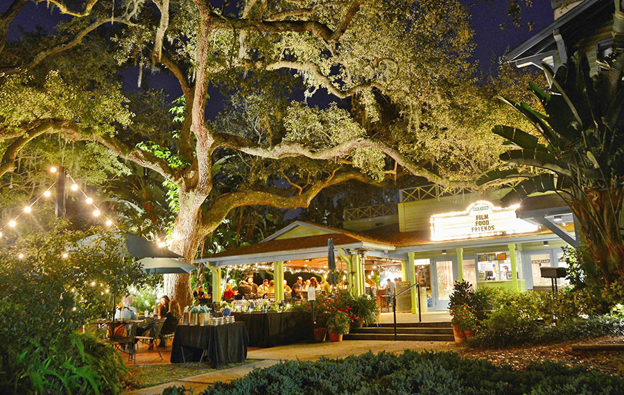 outside patio at night with lighted theater and bar with seating under oak trees enzian theater orlando