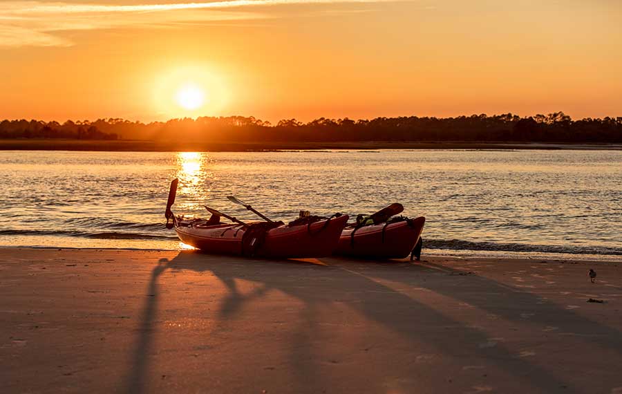 pair of empty kayaks on inlet beach with orange sunrise and long shadows kayak amelia jacksonville