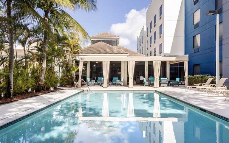 pool area with cabanas and trees along side hotel at hilton garden inn west palm beach airport