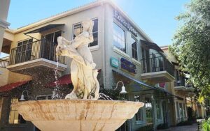 stone woman fountain with rows of stores along avenue at pga commons art dining district palm beach gardens