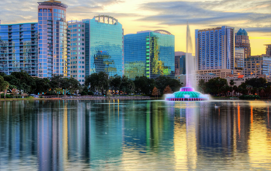 sunset skyline of downtown orlando with colorful fountain and mirrored buildings on west side of lake eola